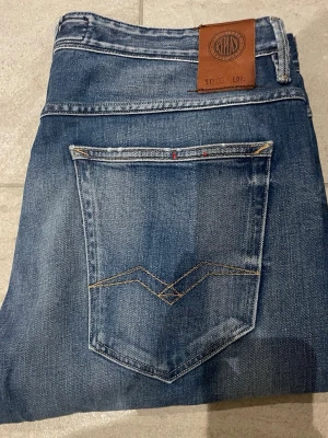 Blå jeans från Replay med skinnpatch - Snygga blå jeans från Replay med klassisk femficksmodell och skinnpatch bak i midjan. Jeansen har diskreta slitningar och kontrastsömmar på bakfickan. Tillverkade i mjuk denim som ger en avslappnad look.