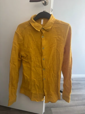 Helt oanvänd gul superskön slimmad skjorta - Snygg gul skjorta i mjuk och luftig bomull med klassisk krage och långa ärmar. Aldrig använd då jag råkade beställa två.  Skjortan har en snygg  passform och stängs med knappar framtill. Perfekt för dig som vill ha en färgklick i garderoben och som vill ha något väldigt bekvämt. Jag har alltid S men denna passade bra pga slimmade passformen.