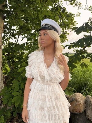 Vit spetsklänning från By Malina - Superfin vit spetsklänning från By Malina med volangdetaljer och v-ringning. Klänningen har korta ärmar och flera lager spets som ger en romantisk känsla. Perfekt till student eller sommarens festligheter!🤍 Klänningen har fortfarande prislappen kvar och är endast testad då jag valde en annan klänning till studenten.