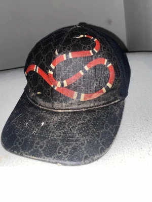 Gucci keps med orm och GG-mönster - Tjena!! Säljer då min keps för att jag inte använder den mer och att vill sälja till en som samlar eller använder kepsar och tycker om de. Kepsen är lite sliten men är äkta , den har lite hårspray i de då förra ägaren som hade använde hårspray och jag tvättade kepsen men de går inte bort har försökt få bort de mesta men det går inte men det är inuti kepsen då man ser ju inte när man använder den men annars är den helt perfekt finns i Skåne !! 