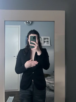 Svart figursydd kavaj med knapp - Snygg svart kavaj med figursydd passform och enkelknäppning framtill. Klassisk krage och långa ärmar. Perfekt för en stilren look och passar till många olika outfits.