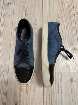 Blå sneakers från Lanvin  - Vi köp innan 30 februari 1700 kr!! Desperat av pengar. Snygga blå sneakers från Lanvin med ovandel i mocka och den svarta cap toan. Skorna har rund tå, snörning och vit sula. Perfekta för dig som gillar stilrena och unika sneakers med premiumkänsla, UK 11. Prisförslag och frågor uppskattas!!