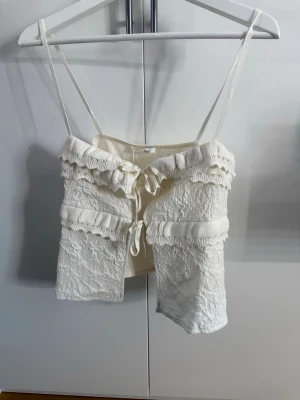 Vit topp  - Supersöt vit topp med tunna axelband, volangdetaljer och knyt framtill. Den är helt oanvänd💕