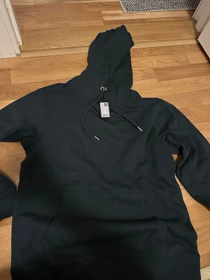 Mörkgrön hoodie med huva stl S - Snygg svart hoodie från Premium Hood i storlek S. Klassisk modell med stor magficka framtill, justerbar dragsko i huvan och ribbade muddar vid ärmar och nederkant. Perfekt för en avslappnad och stilren look.