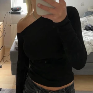 Svart oneshoulder topp Gina Tricot - Trendig svart oneshoulder topp från Gina Tricot i ribbad bomullsmix. Långärmad och croppad modell som sitter tight och framhäver axlarna. Perfekt för dig som vill ha en stilren men ändå unik look.