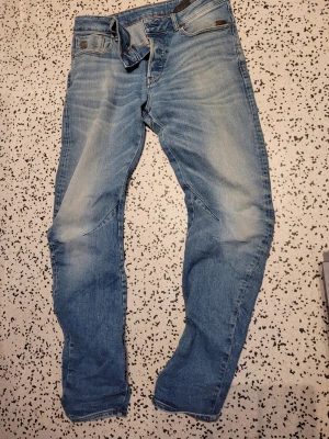 Ljusblå G-Star RAW Arc jeans - Säljer ett par ljusblå G-Star RAW Arc 3D Slim jeans med snygga slitningar och tvättade detaljer. Jeansen har klassisk femficksmodell, knappgylf och är tillverkade i bomull. Perfekta för en avslappnad och trendig look. Width 29 length 32.