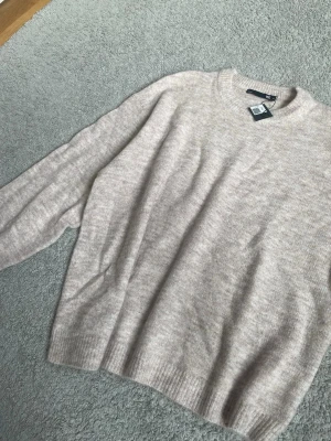 Beige stickad tröja  - Mysig beige stickad tröja med rund halsringning och långa ärmar. Tröjan har en avslappnad passform och ribbade muddar vid ärmslut och nederkant. Perfekt för lager på lager och enkel att matcha till olika outfits. Ny med prislapp 