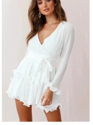 Vit klänning med volanger - Supersöt vit kort omlottklänning med långa ärmar, volangdetaljer och knyt i midjan. Perfekt för sommarens alla tillfällen.                          Använd en gång, så gott som ny och jag köpte den för ca 900kr🫶🏻