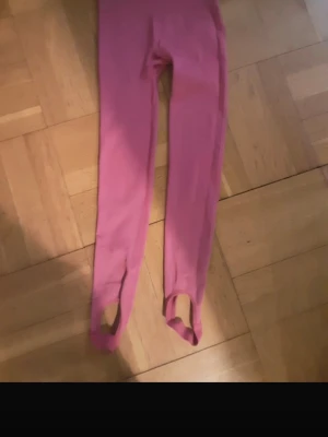 Rosa leggings med fotstrap - Säljer ett par rosa leggings med fotstrap. De har en tight passform och är gjorda i stretchigt material som sitter skönt mot kroppen. Perfekta för dig som vill ha något bekvämt och snyggt till vardagslooken.