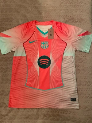Barcelona Nike matchtröja rosa/turkos - Snygg Barcelona matchtröja från Nike i rosa och turkos med klubbmärke och Spotify-logga på bröstet. Tröjan har korta ärmar, rund hals och är tillverkad i ett lätt, ventilerande material perfekt för träning eller match.