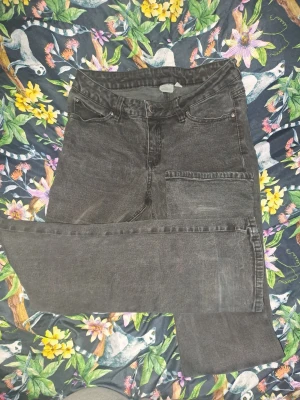 Svarta raka jeans med fickor - Säljer ett par svarta jeans med raka ben och klassisk femficksdesign. Jeansen har en diskret tvättad look och detaljerade sömmar på bakfickorna. Materialet är denim i bomull och de har normal midja. Perfekta till en avslappnad stil.