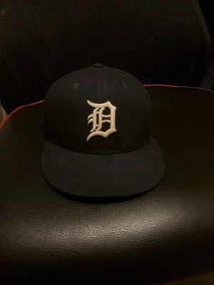 Svart New Era Detroit keps - Snygg svart keps från New Era med Detroit Tigers-logga broderad i vitt framtill. Klassisk flat brim och strukturerad passform. MLB-logga baktill. Perfekt för dig som vill ha en stilren och sportig look.