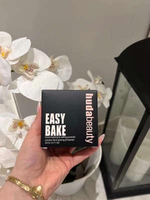 Huda Beauty Easy Bake Setting Powder - Loose baking & setting powder från Huda Beauty i en svart fyrkantig förpackning med vit och rosa text. Perfekt för att fixera foundation och ge en matt finish. Innehåller 20 g puder som passar för att skapa en jämn och hållbar bas.