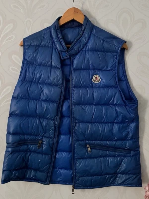 Moncler GUI väst - En stilren Moncler väst i Lblå/babyblå, En size 3a perfekt för att ha över tröjor på vår/sommarkvällar!