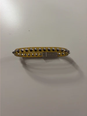 Gult armband med nitar från Coach - Snyggt gult armband från Edblad i läder med silverfärgade nitar längs hela bandet. Armbandet har ett metallspänne med Edblad-logga och en smal, stilren design som ger en edgy touch till din outfit.