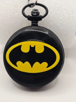 Batman fickur svart och gul "klocka" - Coolt fickur med Batman-loggan i svart och gult. Klockan har en rund form och ett tydligt Batman-emblem på framsidan. Perfekt accessoar för dig som gillar superhjältar och vill sticka ut med din stil.