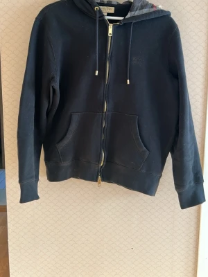 Hoodie från burberry - Hej och välkommen till Liljestrands just nu säljer vi en burberry hoddie !!!!!!äkta!!!!!! Och ovanlig modell pga två dragkedjor och guldiga detaljer nypris runt 5000kr vårt pris endast 1500kr utan några defekter kom med frågor och tveka inte på att höra av er mvh LILJESTRAND