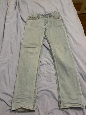 Levi's 501 ljusblå raka jeans - Klassiska Levi's 501 jeans i ljusblå denim med rak passform och fem fickor. Jeansen har knappgylf och ikonisk läderpatch bak i midjan. Perfekta för en avslappnad och tidlös stil.