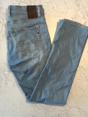 Ljusblå raka jeans från Replay - Säljer ett par ljusblå jeans från Replay med klassisk femficksdesign och raka ben. Jeansen har en snygg läderpatch bak i midjan och diskret Replay-logga på bakfickan. Perfekta till en avslappnad stil och tillverkade i mjuk denim.