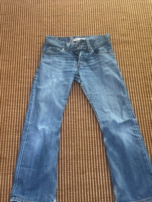 Levi's 512 bootcut jeans blå - Klassiska Levi's 512 jeans i ljusblå denim med bootcut-modell. Jeansen har fem fickor, dragkedja och knapp i midjan samt tydliga slitningar för en cool vintage-look. Perfekta för dig som gillar en avslappnad och tidlös stil. Helt perfekta för den som vill stå ut i mängden nu under sommaren. Pris diskuteras gärna vid snabbt köp😁😁