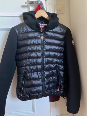 Svart pufferjacka från Colmar BYTE GÅR OCKSÅ - Säljer en svart pufferjacka från Colmar Originals med huva och vadderade paneler. Jackan har svarta ärmar i mjukt material och klassisk Colmar-logga på ena ärmen. Perfekt för kalla vinterdagar och riktigt snygg streetstil.