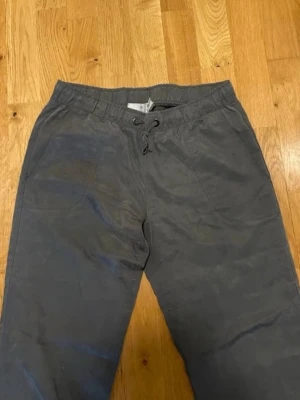 Adidas Grå mjukisbyxor med snörning XSmall  - Snygga grå mjukisbyxor med resår och snörning i midjan. Byxorna har raka ben med muddar och en diskret randig detalj längs bensluten. Perfekta för en avslappnad stil.