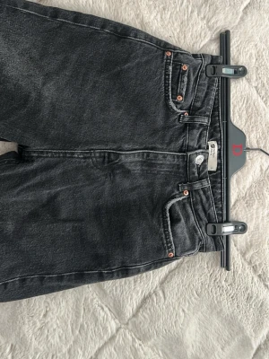 Svarta utsvängda högmidjade jeans från Gina Tricot - Snygga svarta/gråa jeans från Gina Tricot med utsvängda ben och en hög midja, jeansen har även varsin slits på innerbenet. Säljer eftersom dom är för små för mig.