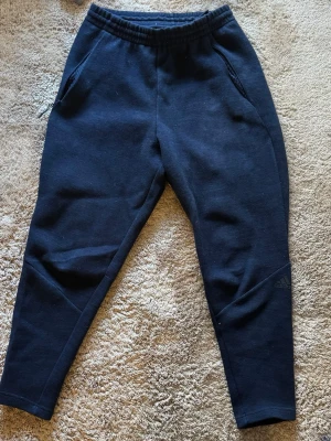 Adidas - Svarta mjukisbyxor från Adidas snygg  passform och elastisk material. Byxorna har två sidofickor och diskret Adidas-logga på ena benet. Perfekta för chill eller träning, tillverkade i mjukt material som känns skönt mot huden.