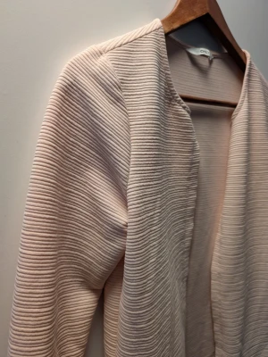 Ljusrosa ribbad cardigan från Only - Ljusrosa cardiganjacka från Only med ribbad struktur och öppen front. Jackan har långa ärmar och en rak, enkel design utan knappar eller dragkedja. Perfekt för lager-på-lager och en stilren look.