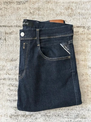Mörkblå jeans från Replay - Snygga mörkblå jeans från Replay med klassisk femficksdesign och kontrastsömmar. Jeansen har rak passform och är tillverkade i ett stretchigt denimtyg som ger en bekväm känsla. Perfekta för dig som gillar stilrena och tidlösa jeans.