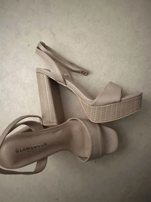 Beige platåsandaler från Glamorous - Snygga beige platåsandaler från Glamorous med breda remmar och justerbart spänne runt ankeln. Skorna har höga blockklackar och en platåsula med diskret mönster. 