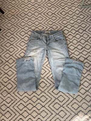 Lågmidjade Levi's 570  straight fit jeans - Ljusblå jeans från Levi's modell 570 Straight Fit med klassisk femficksdesign och slitningar på vänster lår. Jeansen har låg midja och raka ben, perfekt till sommaren. Jeansen är väl använda därav priset. Skriv vid frågor, pris går att diskutera!