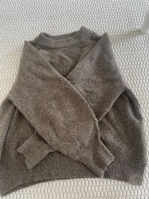 Brun stickad tröja från Pull&Bear - Mysig brun stickad tröja från Pull&Bear med rund halsringning och långa ärmar. Tröjan har en avslappnad passform och är tillverkad i ett mjukt, fluffigt material som känns skönt mot huden. Perfekt för lager-på-lager och chill dagar.