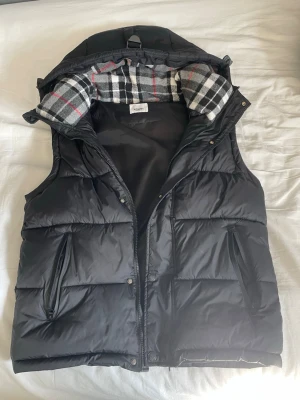 Svart dunväst från Burberry - Svart väst från burberry som också kan bli en jacka på vintern, riktigt snygg vest nu till sommaren och lika fet till vintern. Bara använd fåtal gånger nu i vintras.