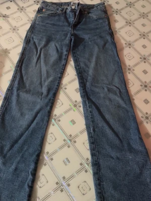 Blå bootcut jeans med fem fickor - Ett par klassiska blå bootcut jeans med fem fickor och normalhög midja. Jeansen har dragkedja och knapp framtill samt bälteshällor. Tillverkade i denim med lätt stretch för skön passform. Perfekta för en avslappnad och trendig look.