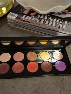 Färgstark ögonskuggspalett med 10 nyanser - Snygg ögonskuggspalett med 10 olika färger i både matta och skimrande nyanser. Paletten innehåller bland annat lila, guld, koppar, rosa, nude och persika. Perfekt för att skapa kreativa och färgstarka ögonmakeuper. Kommer i en svart, rektangulär förpackning med spegel. Väldigt lyxig palett i lyxigt fodral. Kvaliteskuggor. Testad/swatchad.