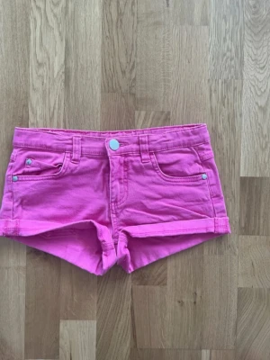 Rosa jeansshorts från KappAhl - Snygga rosa jeansshorts från KappAhl med klassisk femficksmodell och uppvikta benslut. Gjorda i bomullsmix med knapp och dragkedja framtill. Perfekta för sommardagar och ger en färgstark look till din outfit.