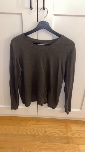 Mörkgrön stickad tröja unisex - En enkel och stilren mörkgrön stickad tröja med rund halsringning och långa ärmar. Tröjan har en rak passform och ribbade muddar vid ärmslut och nederkant. Perfekt att matcha med jeans eller kjol för en avslappnad look.