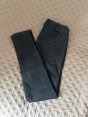 Mörkgrå denimleggings från H&M - Snygga mörkgrå leggings i denimlook från H&M. De har en elastisk midja och en bakficka, vilket ger en avslappnad men ändå trendig stil. Perfekta att matcha med oversized tröjor eller hoodies. Materialet är stretchigt för extra komfort.