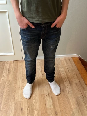 Feta mörkblå slim jeans med slitningar - Modellen är 170cm lång och väger 50kg och midjan var en aning för stor för han! Snygga mörkblå jeans med slim passform och diskreta slitningar framtill. Jeansen har klassisk femficksdesign och är tillverkade i bomull med en skön stretch. Perfekta för en avslappnad och trendig look.