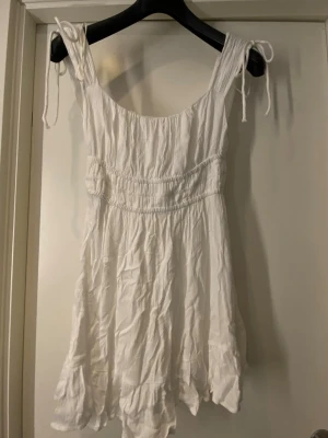 Vit sommarklänning  - Vit klänning ifrån Bershka med knytband på axlarna och volangkant nedtill. 