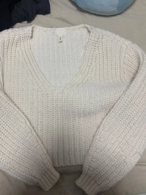 Vit stickad tröja från H&M - Mysig vit stickad tröja från H&M med grovstickat mönster och djup v-ringning. Tröjan har långa ärmar och ribbade muddar vid ärmslut och nederkant. Perfekt för lager-på-lager och chill dagar.