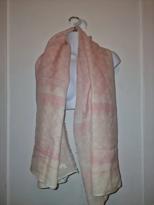 Rosa sjal från By Malene Birger - En elegant sjal med ett diskret mönster i ljusa nyanser. Sval och lätt, perfekt att svepa runt sig. Tunt vävt ull med diskret mönster och fransad kant. Enkel att styla till olika outfits.