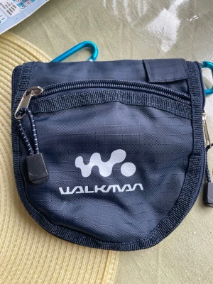 Blå Walkman väska med dragkedja - Snygg blå väska från Walkman i slitstark nylon med dragkedja framtill och flera fack inuti. Väskan har ett justerbart band och karbinhake för enkel upphängning. Perfekt för småprylar och accessoarer när du är på språng.