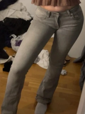Grå bootcut jeans med låg midja - Säljer ett par grå bootcutjeans och låg midja. Jeansen har klassisk femficksdesign och stängs med knapp och dragkedja. Säljer för att de blivit för små för små för mig.