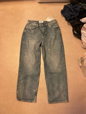 Blå raka jeans med slitningar - Säljer ett par blå jeans med raka ben och lätt slitna detaljer. Jeansen har klassisk femficksdesign och hög midja. Materialet är denim och färgen är en tvättad ljusblå nyans. Perfekta för en avslappnad och trendig look.