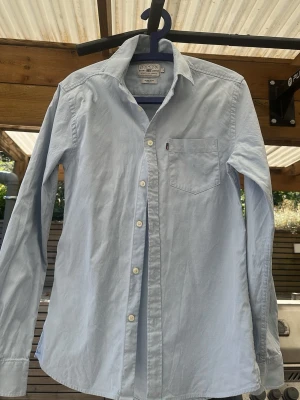 Ljusblå skjorta från Lexington - Klassisk ljusblå skjorta från Lexington med bröstficka och vita knappar. Skjortan har en tidlös design med button down-krage och är tillverkad i mjuk bomull. Perfekt för en clean och avslappnad stil.