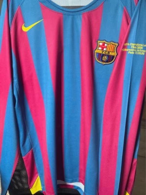 Barça långärmad matchtröja blå/röd - Långärmad FC Barcelona matchtröja med blå och röda vertikala ränder, klubbmärke på bröstet och gul Nike-logga. Text om Champions League-finalen 2006 broderad på bröstet. Tillverkad i funktionsmaterial, perfekt för fotbollsträning.