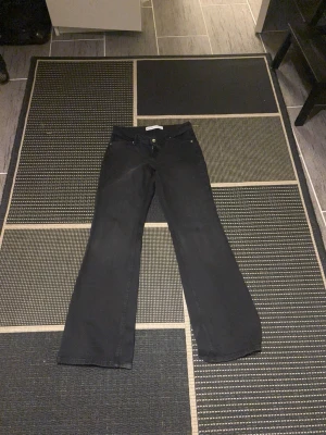 Svarta bootcut jeans med hög midja, bershka - Säljer ett par svarta jeans med bootcut-modell och hög midja. Jeansen har klassisk femficksdesign och stängs med knapp och dragkedja. Materialet är denim med lite stretch för skön passform. Perfekta för dig som gillar en retro och avslappnad stil.
