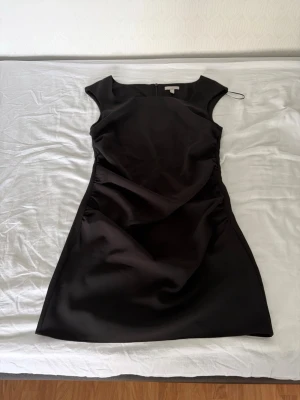 Svart kortärmad klänning - En stilren svart klänning med korta ärmar och rund halsringning. Klänningen har en figurnära passform och är sydd i ett slätt material som ger en elegant look. Perfekt för dig som gillar minimalistisk stil.